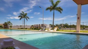 Une piscine avec des chaises longues, des palmiers et un ciel dégagé.