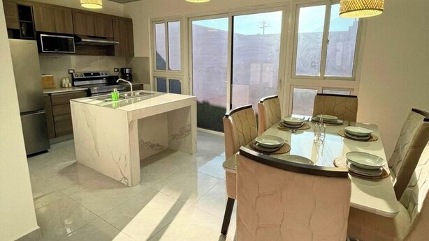 Une cuisine moderne dotée d’un îlot central, d’un coin repas avec une table et des chaises, et d’un éclairage suspendu.