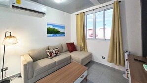 Un salon moderne comprenant un canapé, une table basse, une lampe, un climatiseur, une fenêtre avec des rideaux et un tableau accroché au mur.
