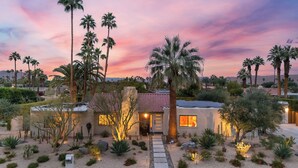 A desert-style house with a patio, palm trees, and a sunset sky. - Design-forward Palm Springs Home w/ Saltwater Pool, Lush Yard & Multiple Outdoor Dining Areas Casa Papagayo by Avantstay (Palm Springs)