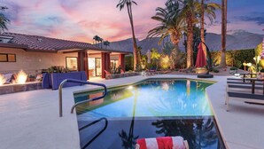 A pool with a clear view of the mountains in the background, a covered patio area, and a fire feature. - Design-forward Palm Springs Home w/ Saltwater Pool, Lush Yard & Multiple Outdoor Dining Areas Casa Papagayo by Avantstay (Palm Springs)