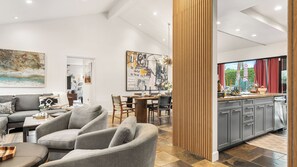 Uma sala de estar moderna com sofá, cadeiras, mesa de jantar e área de cozinha com armários e uma janela.