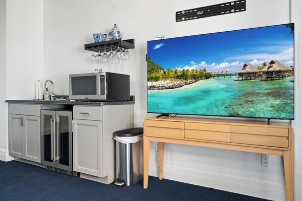 Una cocina moderna con armarios grises, un refrigerador de acero inoxidable, un microondas y un televisor sobre un soporte de madera.