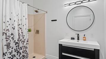 A bathroom with a shower, a sink with a mirror, and toiletries on the counter.