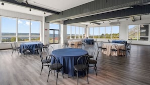A spacious indoor area with round tables and chairs, large windows offering views of the landscape, and a high ceiling with exposed beams.