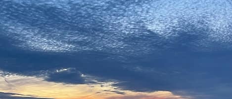 A sunset view from a balcony with a railing, overlooking a landscape with distant buildings.