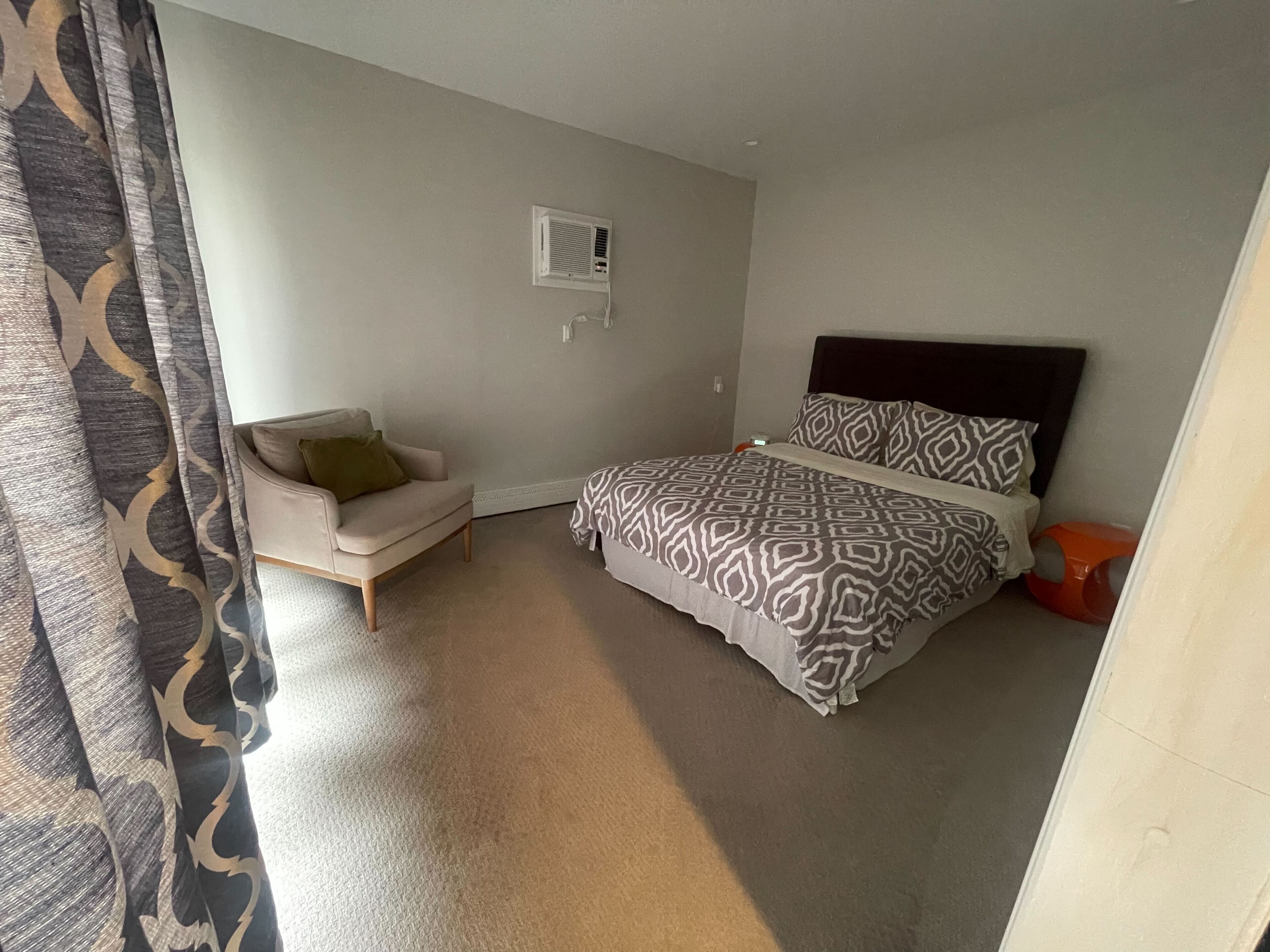 Een slaapkamer met een bed, een stoel, een nachtkastje en een wandairconditioner.