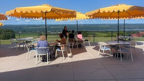 An outdoor patio with tables and chairs under yellow umbrellas, overlooking a scenic landscape.