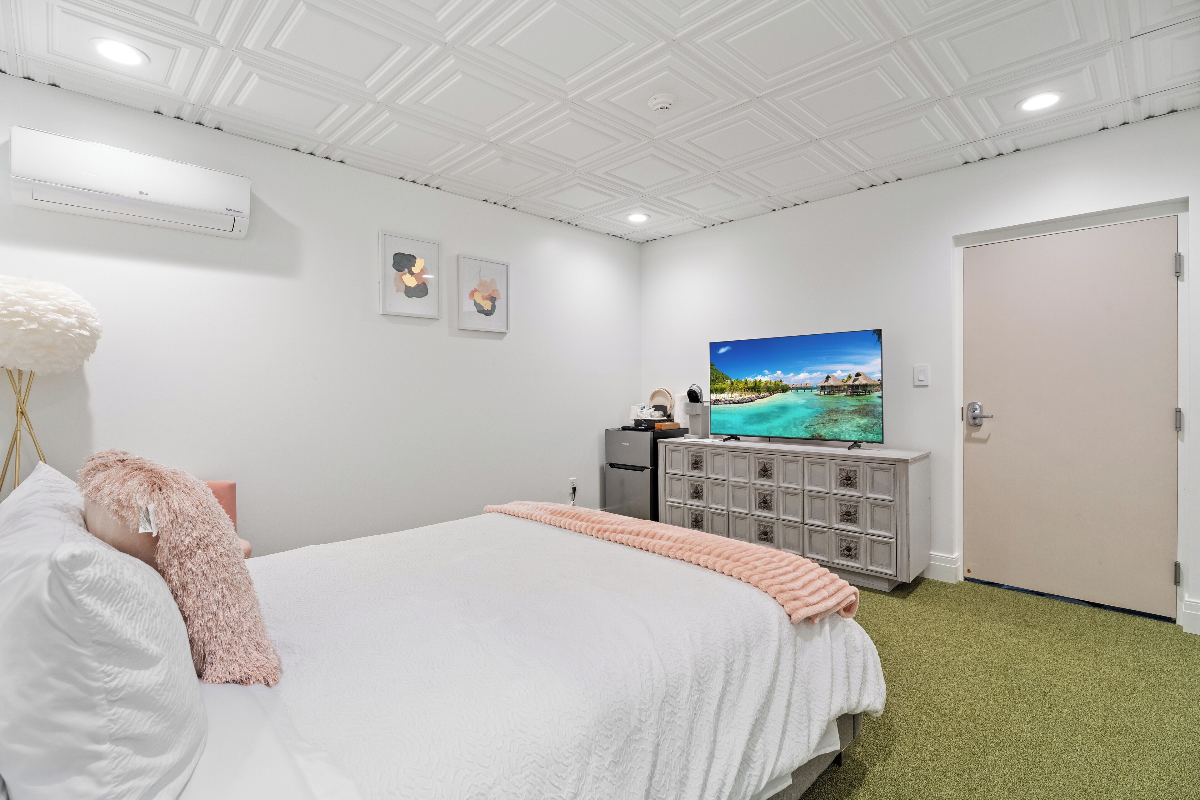 A hotel room with a large bed, a television on a dresser, a white air conditioner, and a door.