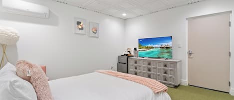 Hotellihuone, jossa on suuri sänky, televisio lipaston päällä, valkoinen ilmastointilaite ja ovi.