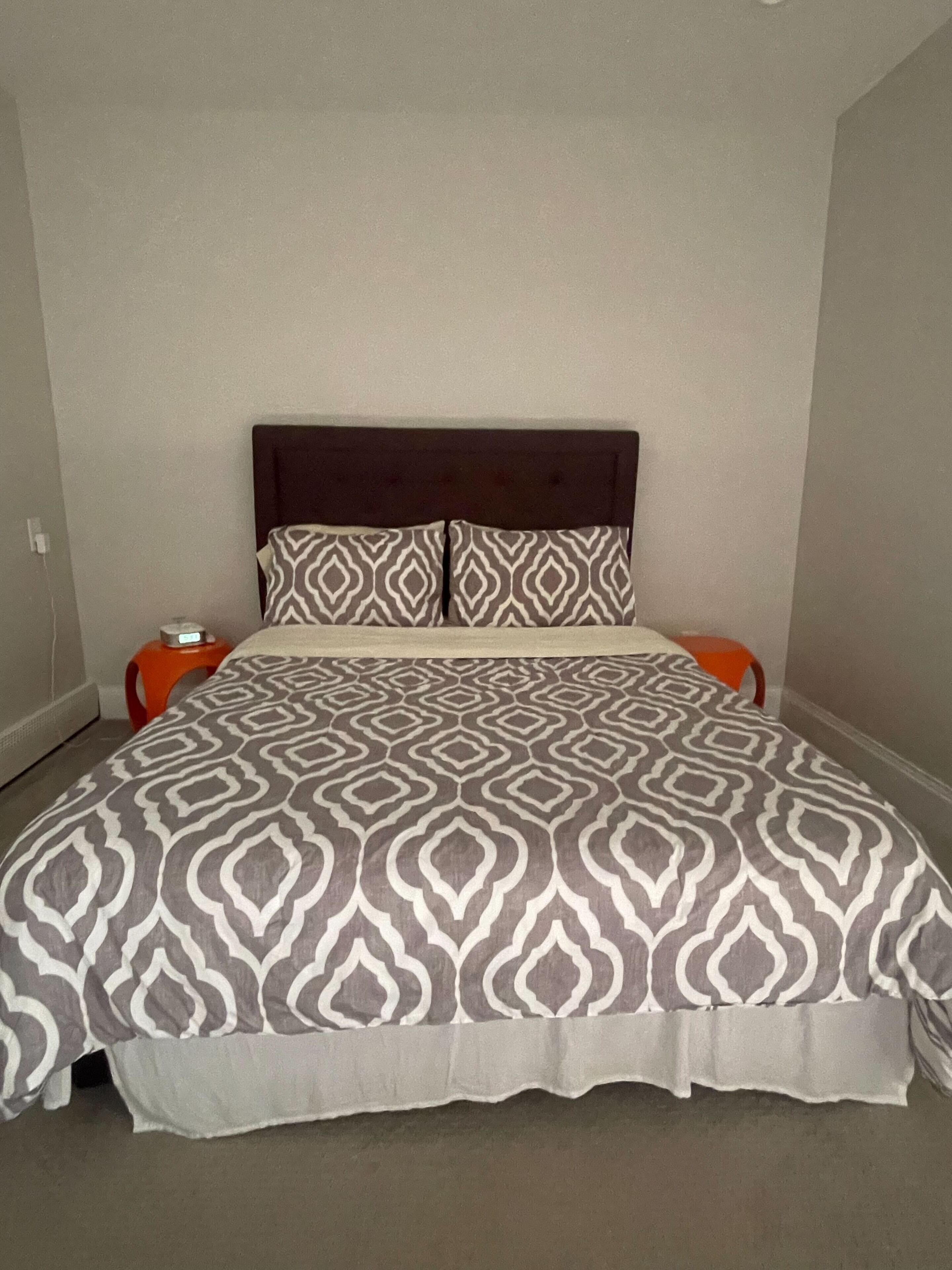 Ein Bett mit einem gemusterten Überwurf und zwei Kissen, das von zwei Nachttischen mit Lampen flankiert wird.