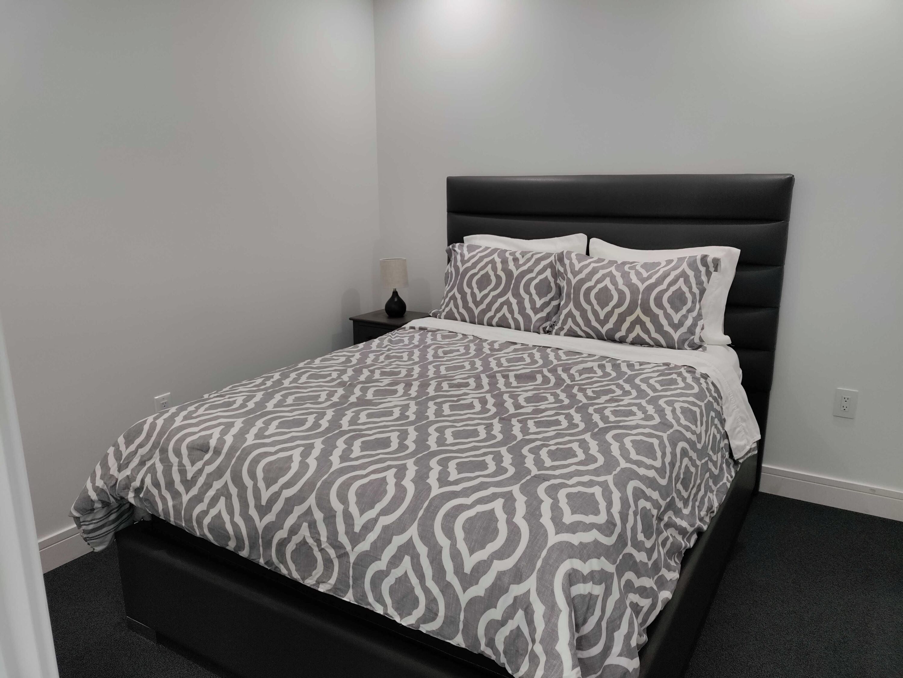 A neatly made bed with a patterned bedspread and matching pillows, a black headboard, and a small bedside table with a lamp.