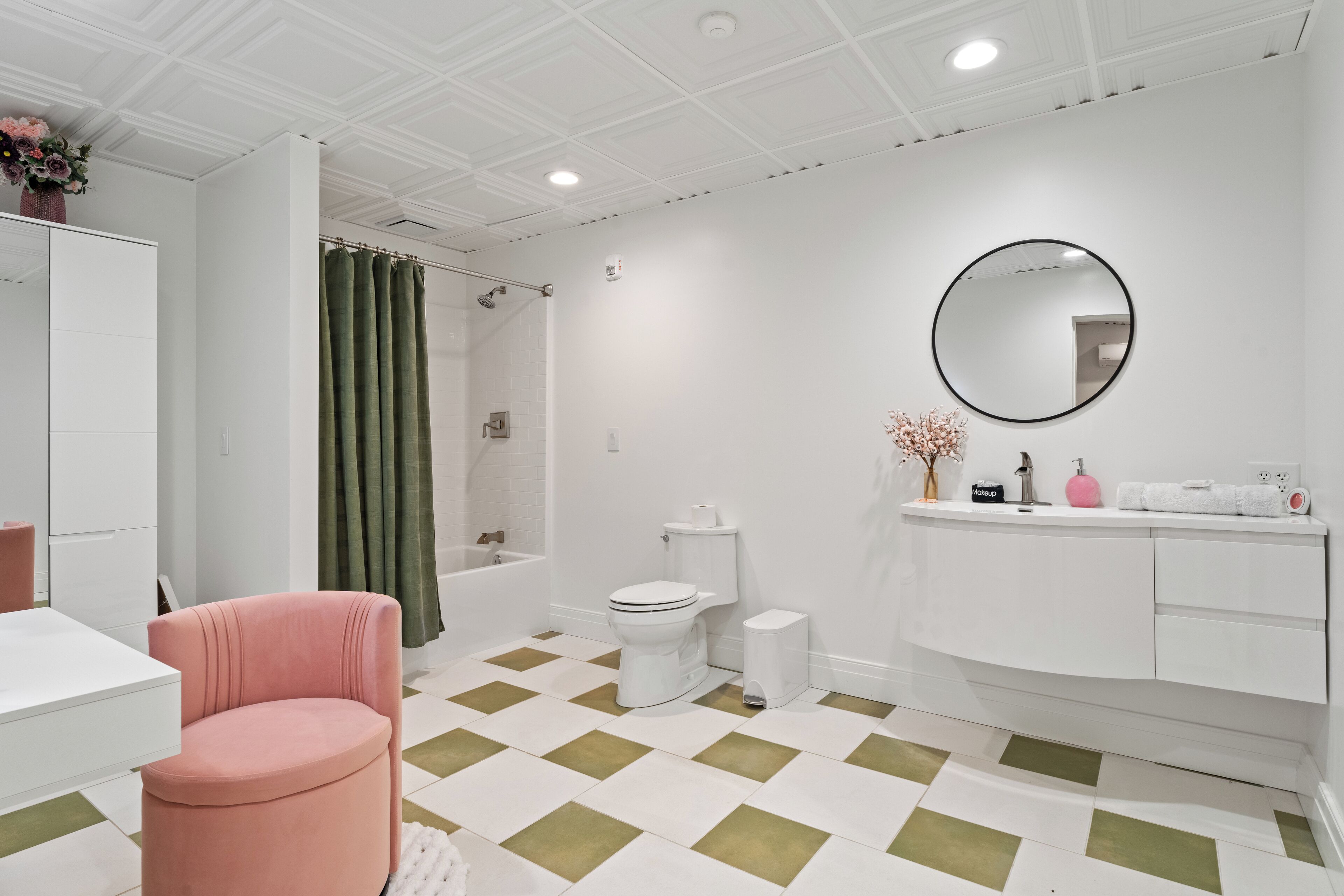 Ein modernes Badezimmer mit einem weißen Waschtisch, einem runden Spiegel, einer Toilette und einer Dusche mit grünem Vorhang.