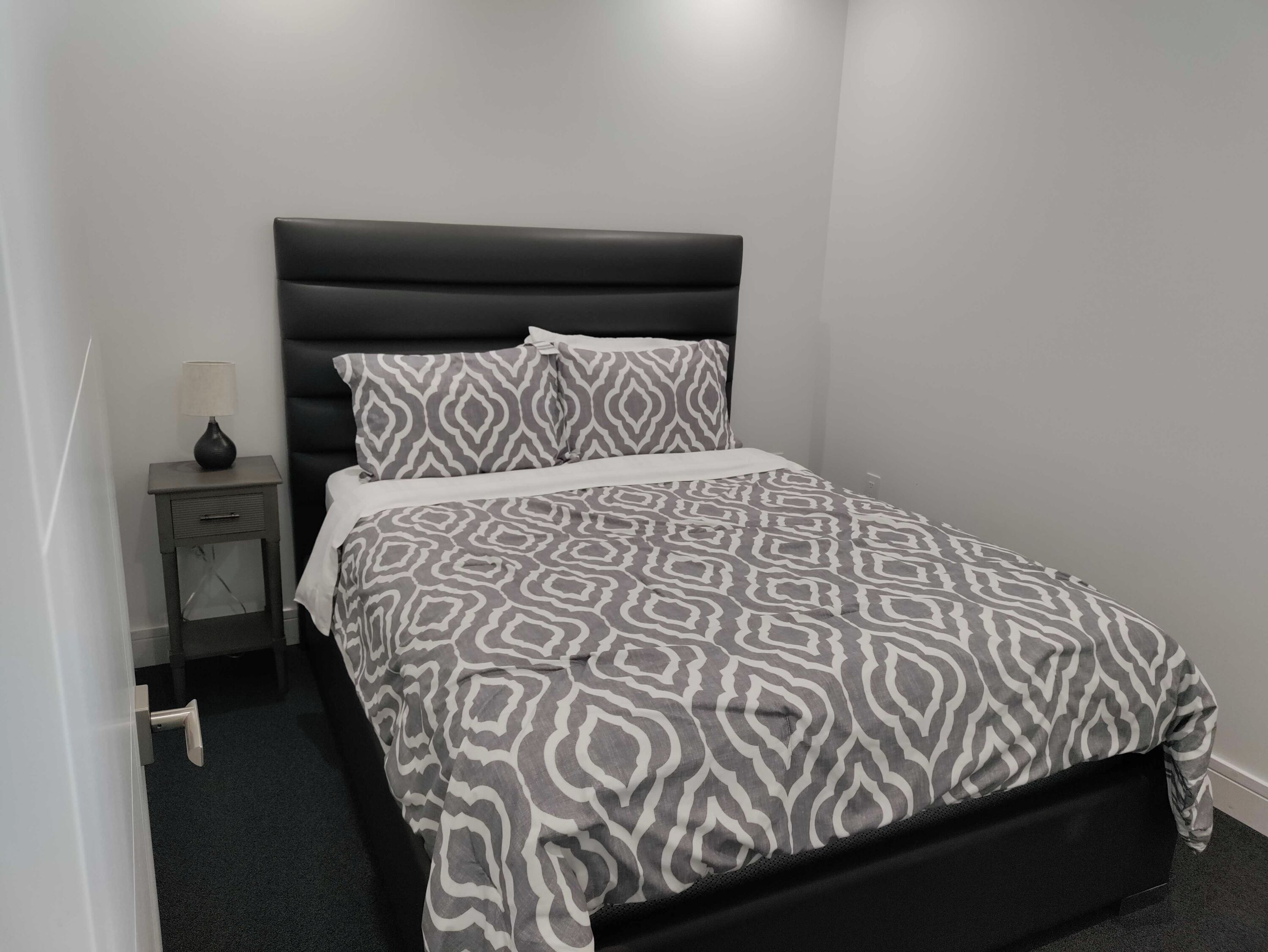 A bedroom with a black headboard, a patterned bedspread, and a bedside table with a lamp.