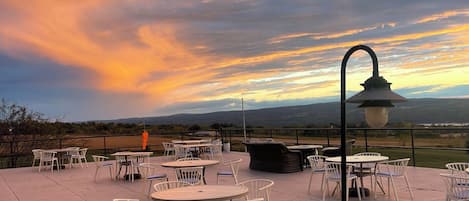 An outdoor patio with tables and chairs, a lamp post, and a scenic view of the landscape.