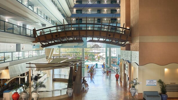 A multi-level atrium with a glass bridge, potted plants, and a pool area. - Sunlit 1-Bedroom Apt at Crown Tower with Parking (Surfers Paradise)