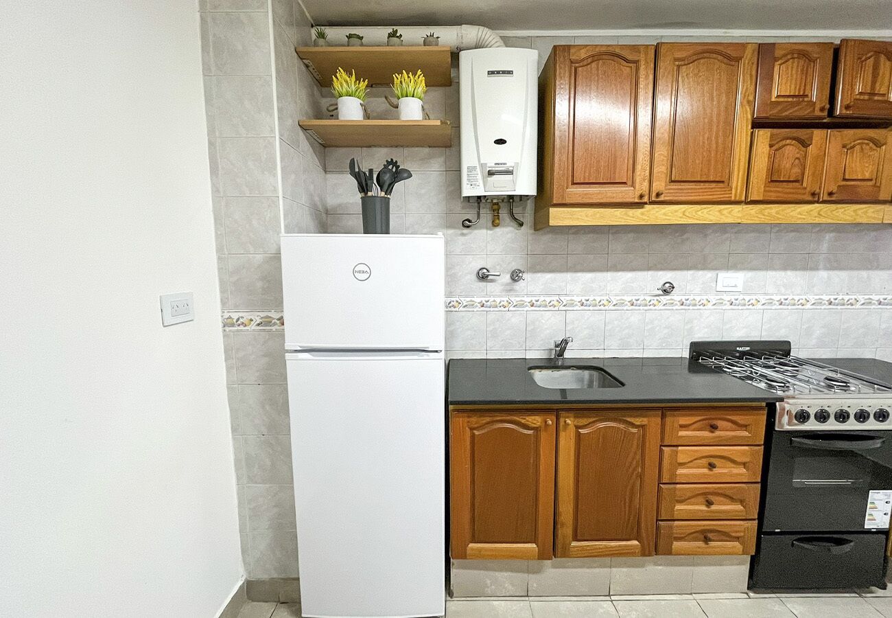 Una cocina con armarios de madera, un refrigerador blanco, una estufa negra y un lavamanos.