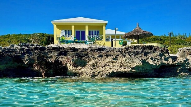 A yellow building with a thatched roof structure on a rocky outcrop, overlooking clear turquoise water. - Newly Remodeled Estate Directly on the Calm Caribbean w/Pool, Views (Current)