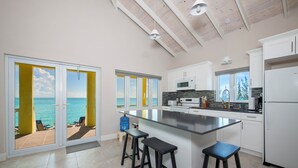 A modern kitchen with a large island, white cabinets, and a view of the ocean. - Newly Remodeled Estate Directly on the Calm Caribbean w/Pool, Views (Current)
