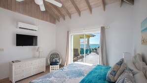 A bedroom with a bed, a TV, a ceiling fan, a window with a view of the ocean, and a balcony with chairs. - Newly Remodeled Estate Directly on the Calm Caribbean w/Pool, Views (Current)