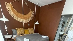 Un dormitorio con una cama, una lámpara colgante, una mesita redonda y suelo de baldosas.