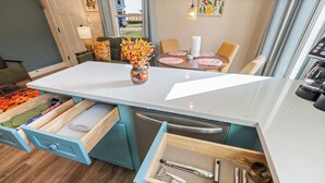 Een moderne keuken met een centraal eiland, houten lades en een eethoek met een tafel en stoelen.