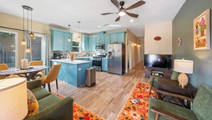 Een moderne keuken met blauwgroene kastjes, een centraal eiland en een eethoek met groene stoelen.