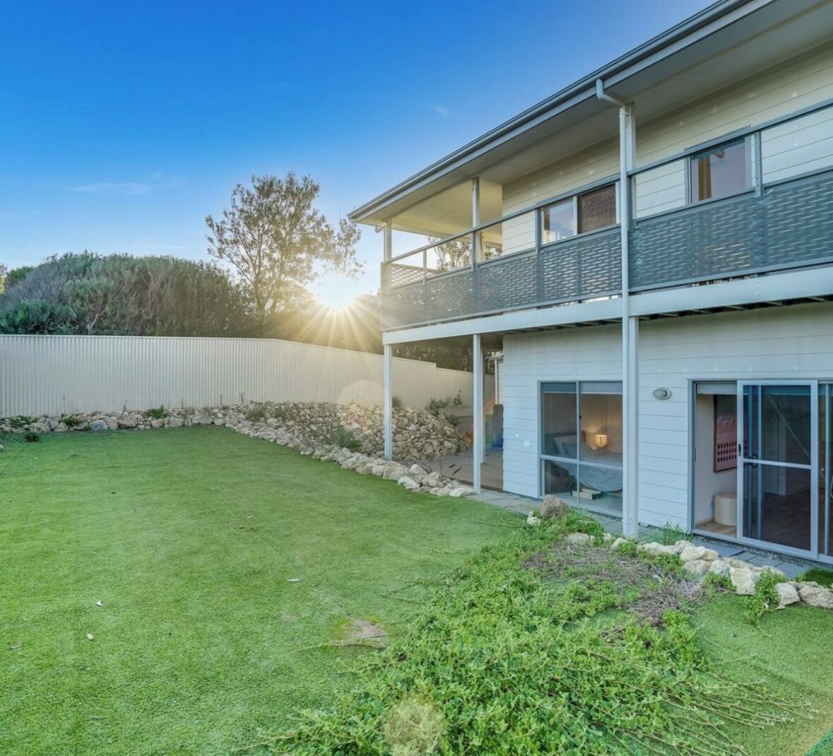 Une maison moderne à deux étages, dotée d’une pelouse bien entretenue et d’un mur en pierre.
