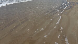 Ein Strand mit breitem Sandstrand, sanfte Wellen, die am Ufer schlagen, und ein klarer Himmel mit vereinzelten Wolken.