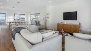 Ein geräumiges Wohnzimmer mit einer großen Sofagarnitur, einem Holzkasten und einem flachbildfernseher an der Wand.