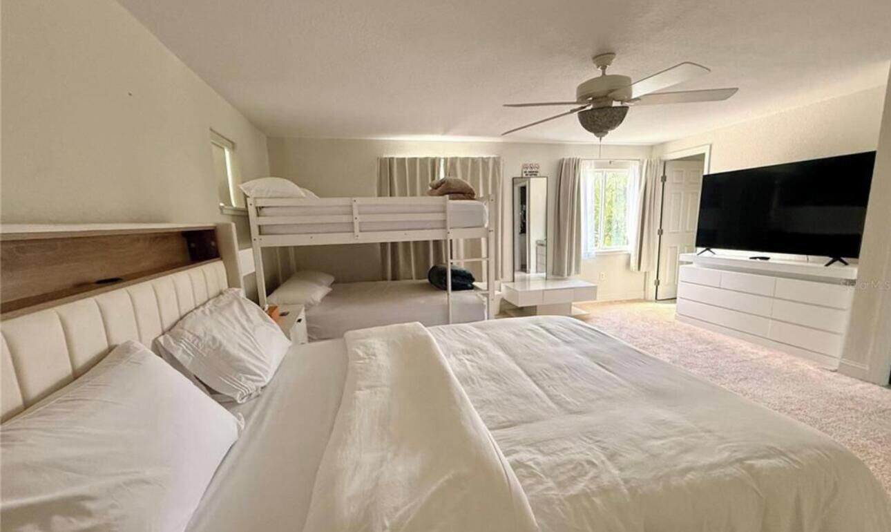 Ett hotellrum med en våningssäng, ett skrivbord med en stol, en tv och en takfläkt.