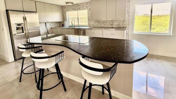 Una cucina moderna con isola a forma di arco, sgabelli da bar e una grande finestra.