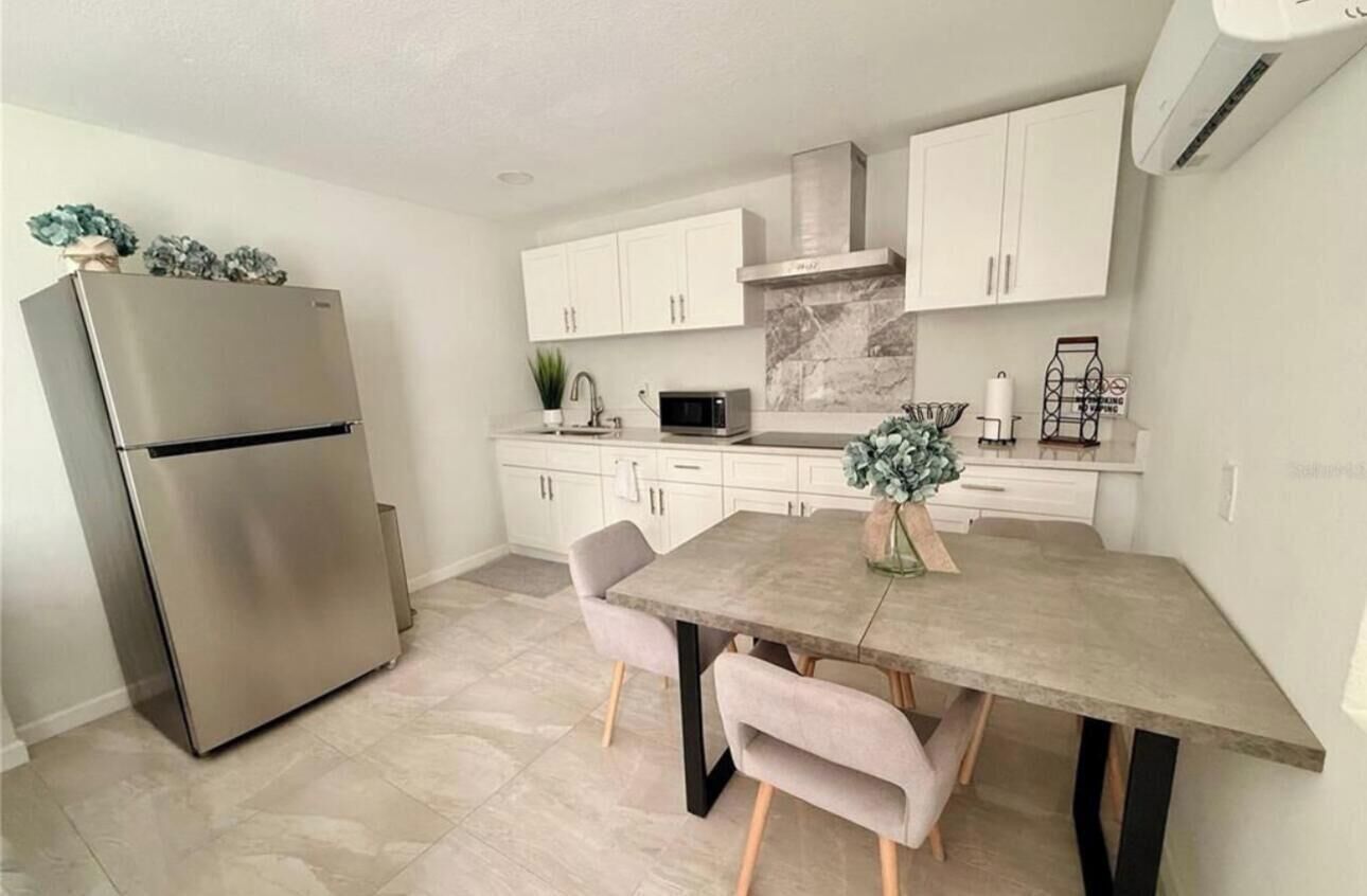 A modern kitchen with white cabinets, a stainless steel refrigerator, a marble backsplash, and a dining table with chairs.