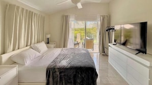 Una camera d'hotel moderna con un letto grande, una ventola a soffitto, una TV e vista all'esterno tramite una porta scorrevole in vetro.