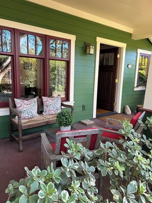 Un porche avec un banc en bois et une petite table, des murs verts et une porte.