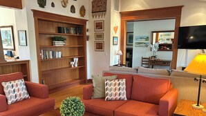 Una sala de estar acogedora con un sofá rojo, sillones a juego, una mesa de centro de madera y una estantería llena de libros y objetos decorativos.