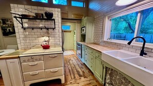 A kitchen with a wooden floor, white cabinetry, and a window overlooking a backyard. - 2-bedroom house walking distance to downtown Grand Haven (Grand Haven)