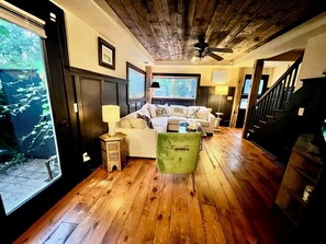 A cozy living room with wooden flooring, a green chair, a white sofa, and a staircase leading to another level. - 2-bedroom house walking distance to downtown Grand Haven (Grand Haven)