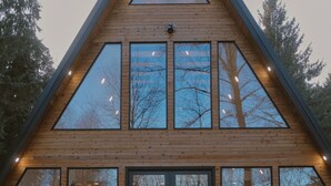 Een moderne houten chalet met grote ramen, een dakraam in het midden en een zichtbaar interieur met meubels.