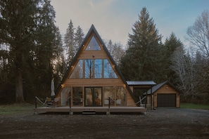 A modern wooden cabin with a triangular roof, large windows, and a covered deck area. - Unique A-Frame house nestled at the edge of rainforest with Sauna & Hot-tub (Forks)