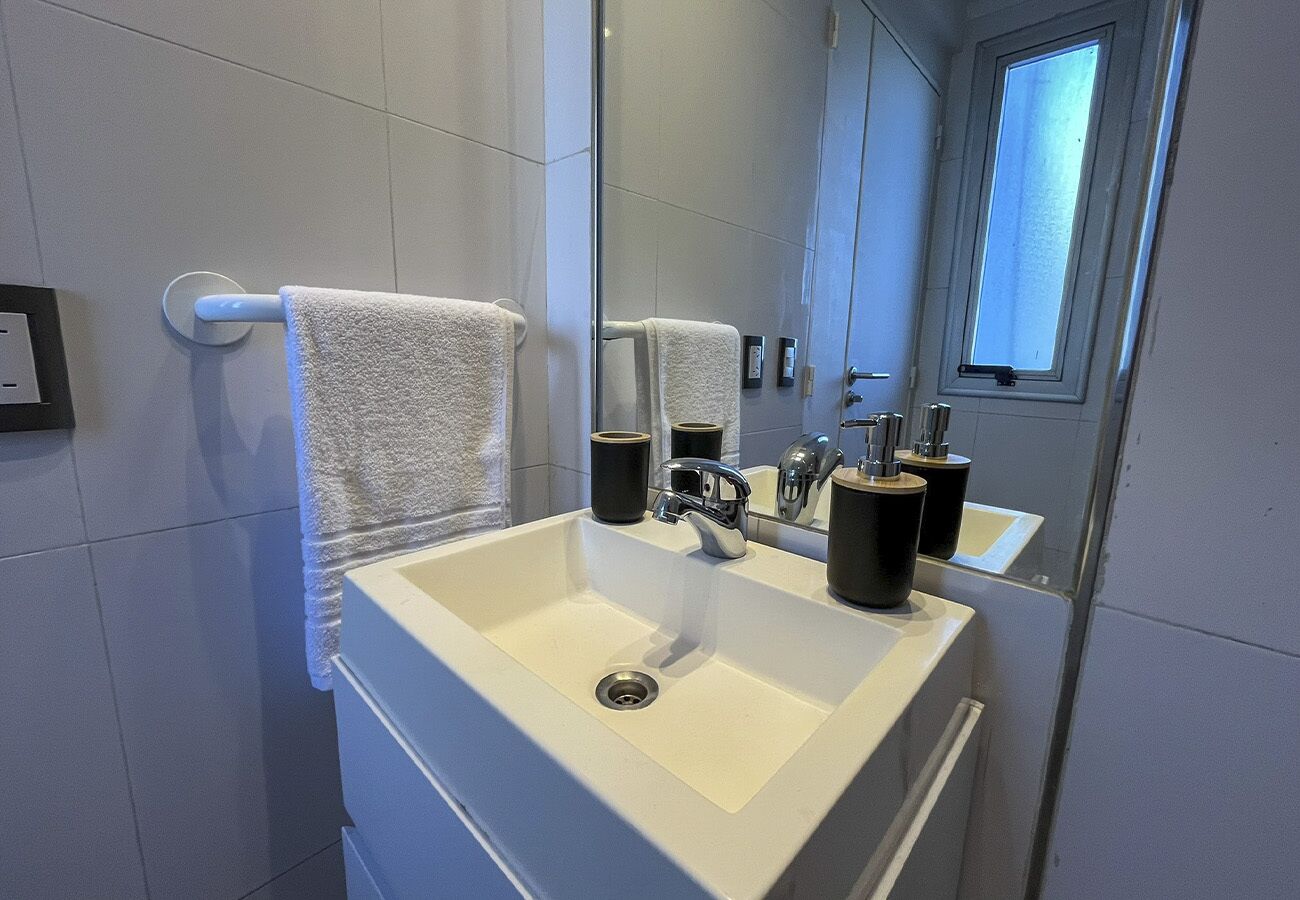 A modern bathroom with a white sink, two black soap dispensers, and a towel rack with a white towel.