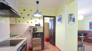 A compact kitchen with a stove, oven, and a small refrigerator. There is a red trash bin and a ceiling light fixture. - Holiday apartment with air conditioning (Pula)