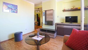 A living room with a glass coffee table, a sofa with a red cushion, a TV on a wooden cabinet, and a painting on the wall. - Holiday apartment with air conditioning (Pula)