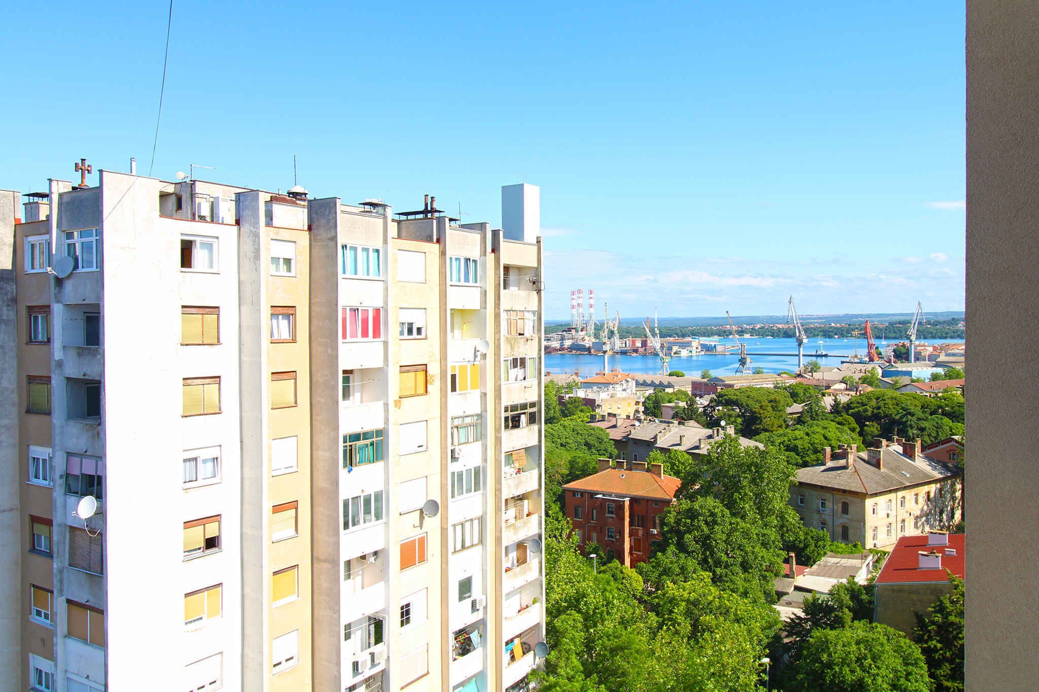 A high-rise building with multiple balconies, a view of a harbor with boats, and a mix of residential and commercial buildings.