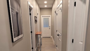 Un couloir avec un plancher en bois, des portes blanches et un tableau encadré accroché au mur.
