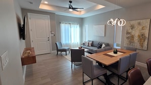 Un salon moderne comprenant un coin repas, un ventilateur de plafond et un grand tableau abstrait.