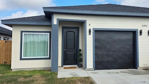 Une maison moderne à deux étages, avec une porte d’entrée sombre, un grand portail de garage et une boîte aux lettres située sur le côté droit.