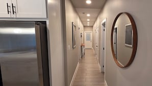 Un couloir avec un réfrigérateur en acier inoxydable, des tableaux encadrés accrochés aux murs et un plancher en bois.