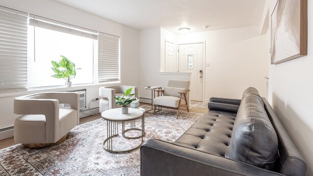 A modern living room with a black leather sofa, a white armchair, a round coffee table, and a patterned rug.