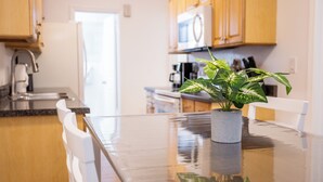 A kitchen with wooden cabinets, a microwave, and a potted plant on a reflective glass table.